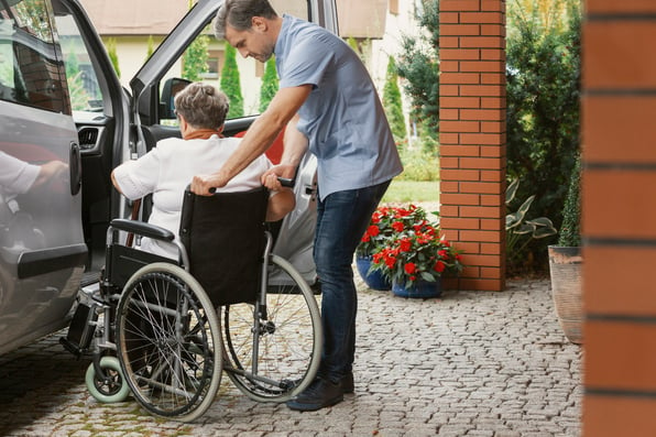 Man helping woman in a wheelchair get into a vehicle